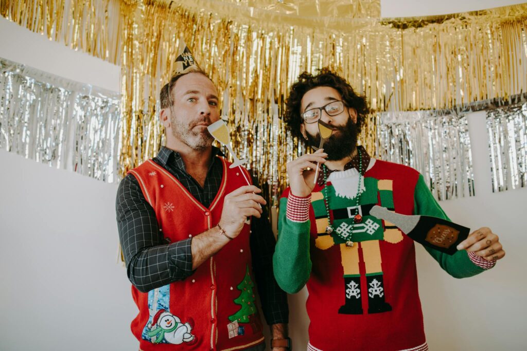 Two men enjoying a holiday party with fun ugly Christmas sweaters and cheerful decorations.
